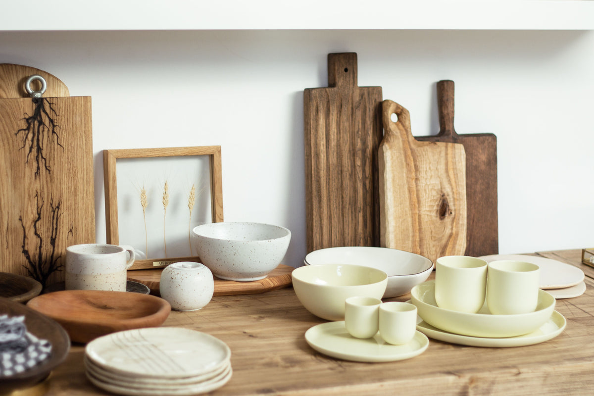 Set of ceramic bowls, cups, and wooden cutting boards on a wooden surface.